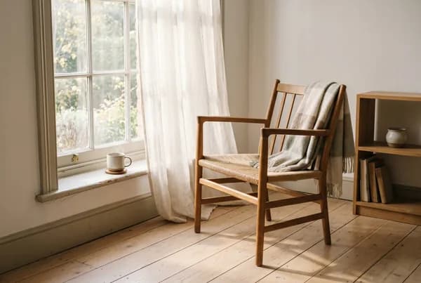 An empty wooden reading chair in soft morning window light, a wool throw and a cup of tea on the sill - on presence and coming back to your own life, with Ellie James