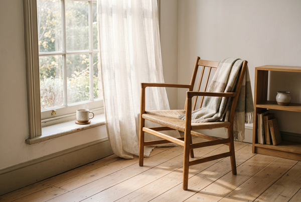 An empty wooden reading chair in soft morning window light, a wool throw and a cup of tea on the sill — on presence and coming back to your own life, with Ellie James